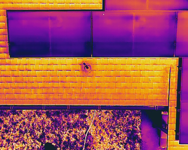 Thermal drone inspection of residential rooftop solar panels showing temperature variations — hot spots and underperforming cells visible in orange and purple